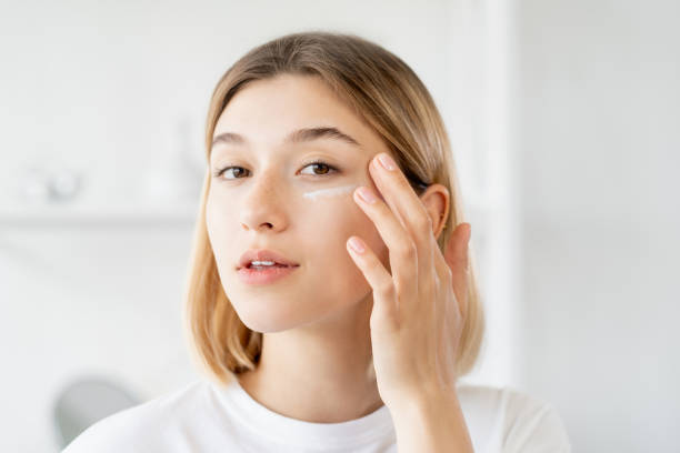 Young woman applying facial skincare product in a bright, clean bathroom setting.