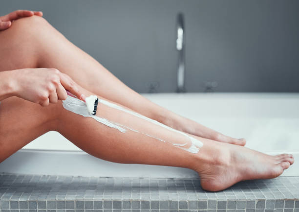 Close-up of a woman shaving her legs in the bathroom, focusing on smooth skin care and hygiene routine.