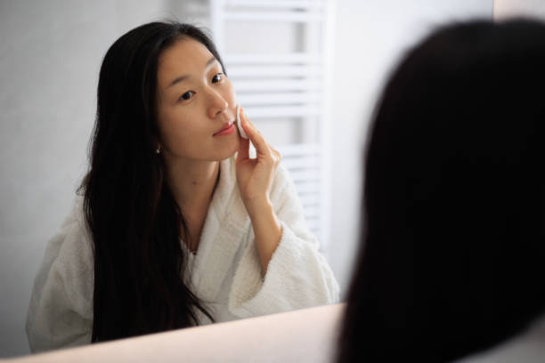 Woman applying skincare products in front of mirror